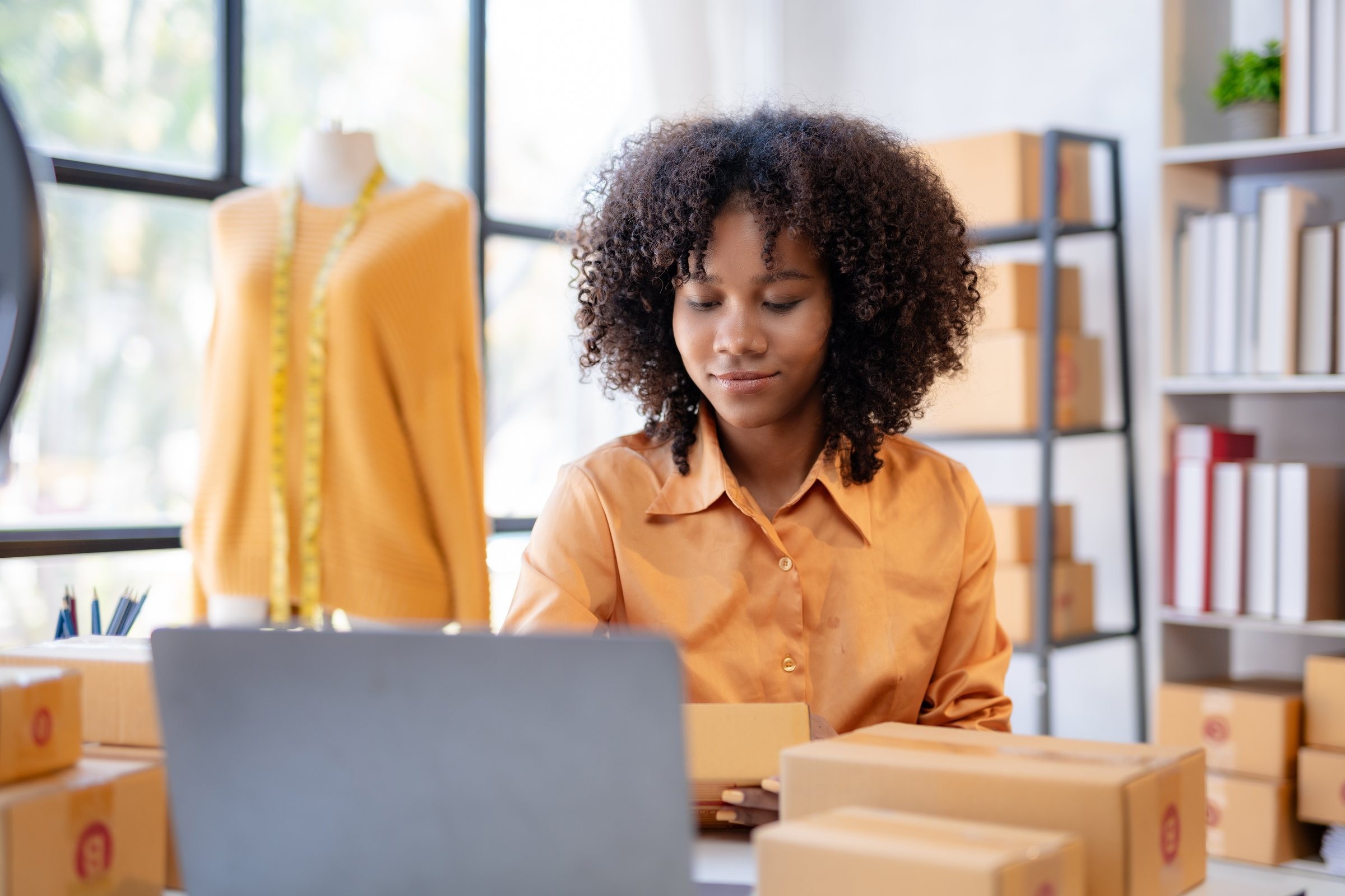 A young business owner at her laptop among order boxes