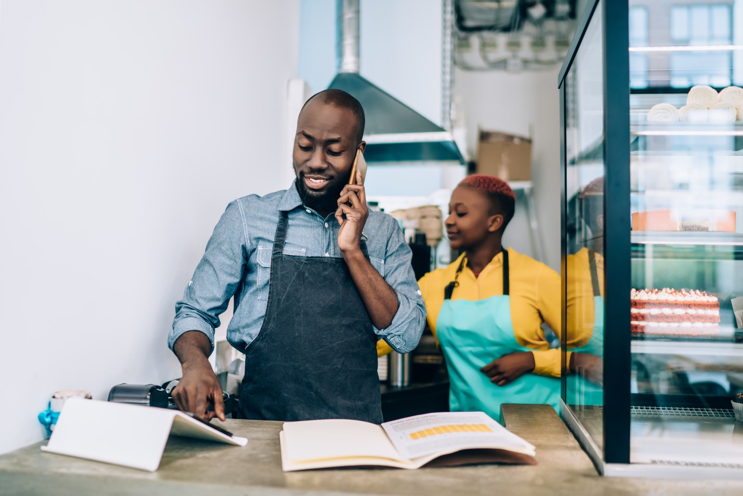 A pastry-shop owner taking an order by phone, a colleague behind him